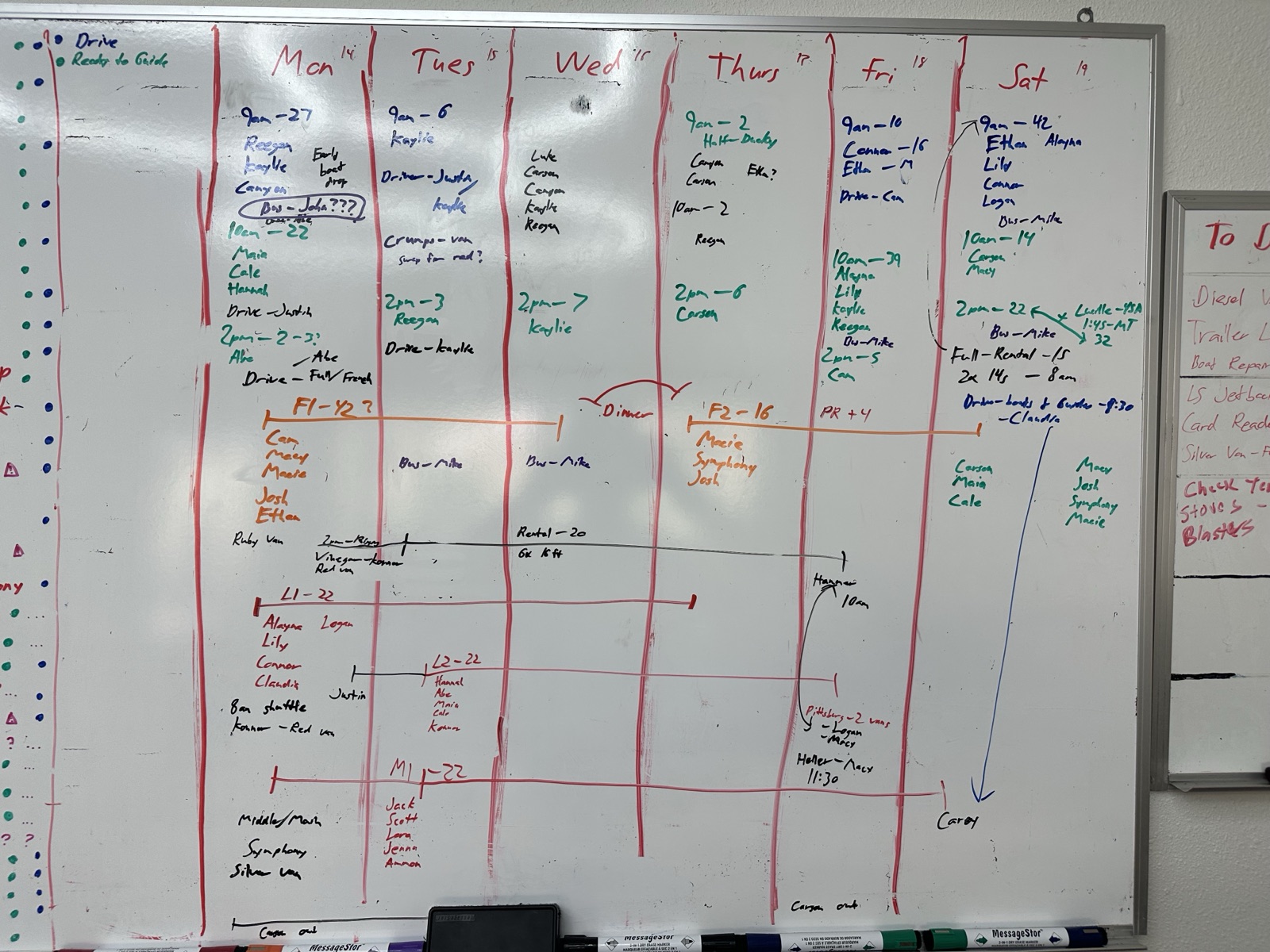 A wall-mounted whiteboard holding one week of rafting operations in hand-written marker: columns for Monday through Saturday, launch times with guest counts, crew assigned per trip, driver and van assignments, and colored lines tracking multi-day trips across days.
