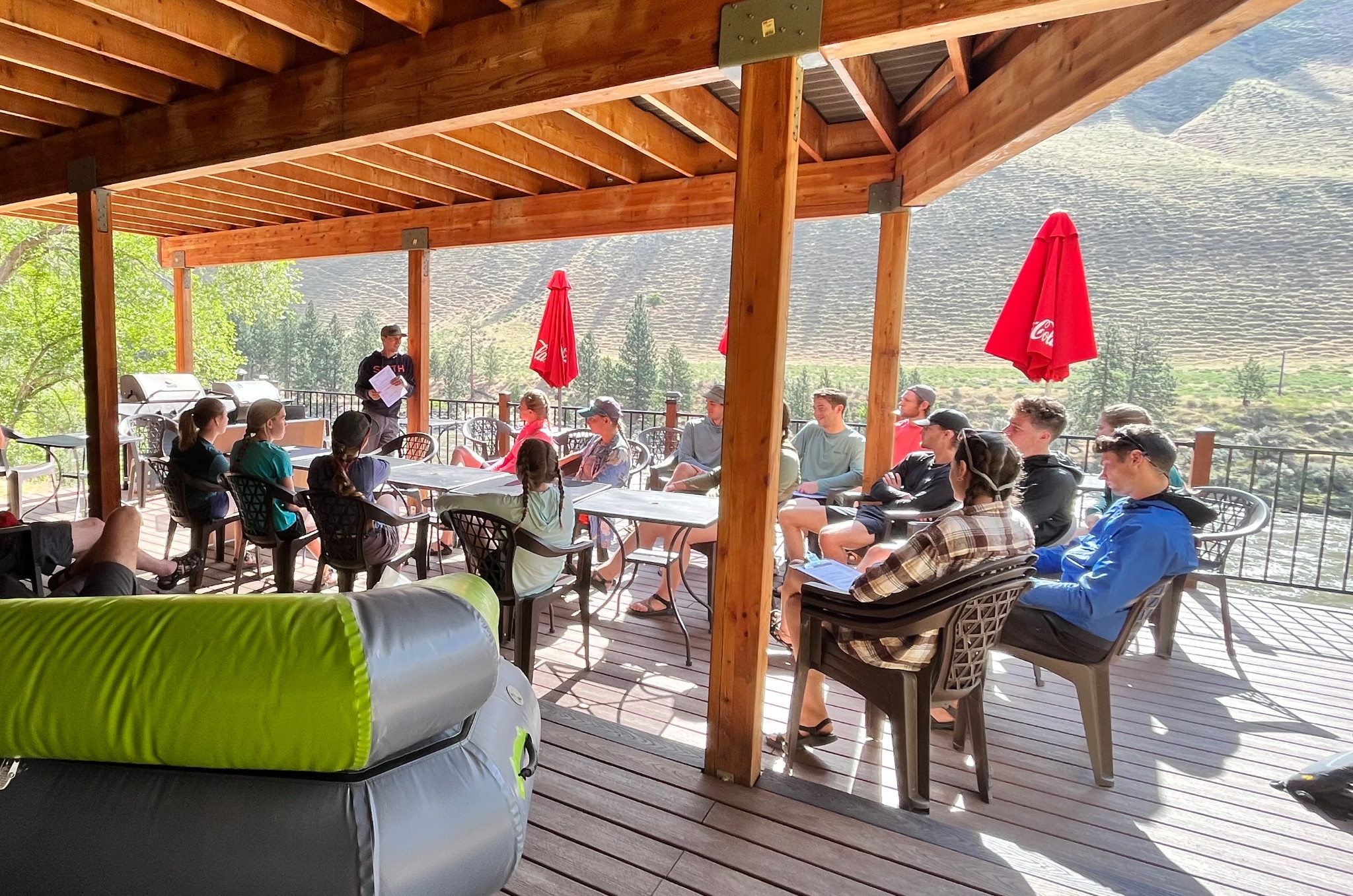 Justin Smith briefing the Adventure Idaho team around tables on an outdoor deck.